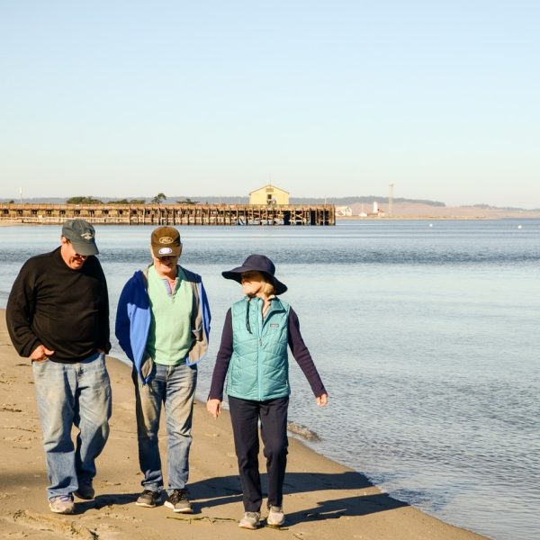 A woman and two men walk side-by-side along the beach in Jefferson County, Washington.